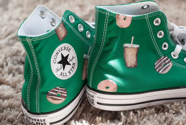 Green Converse All Star shoes with donut and coffee cups painted on on a carpeted floor.