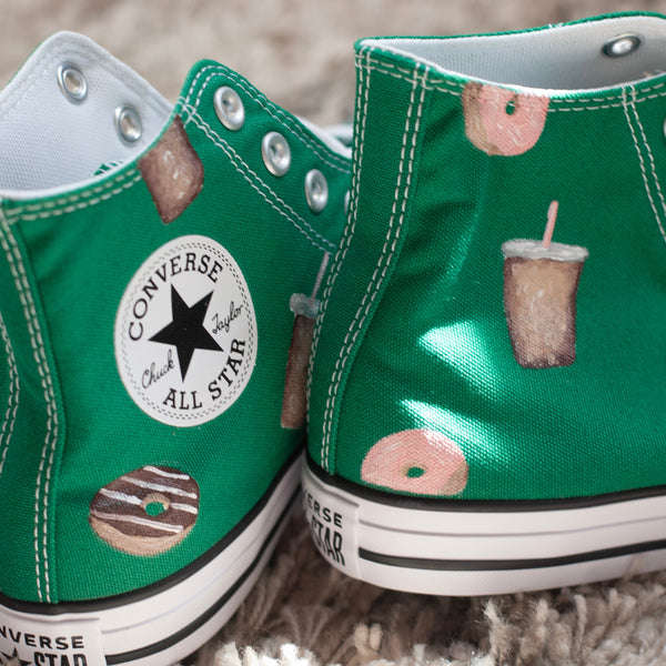 Green Converse All Star shoes with donut and coffee cups painted on on a carpeted floor.