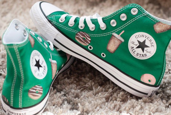 Green Converse All Star shoes with donut and coffee cups painted on on a carpeted floor.