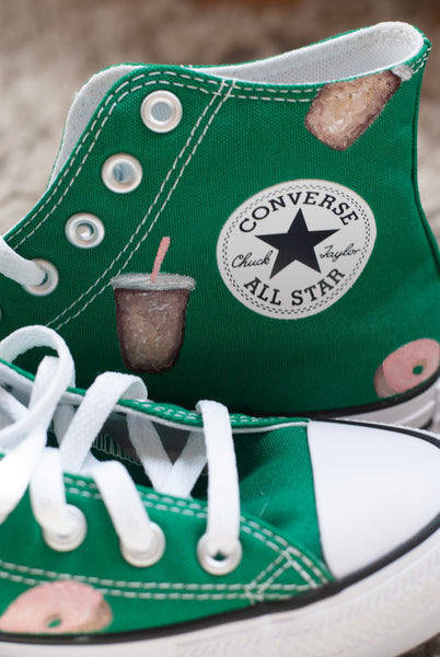Green Converse All Star shoes with donut and coffee cups painted on on a carpeted floor.