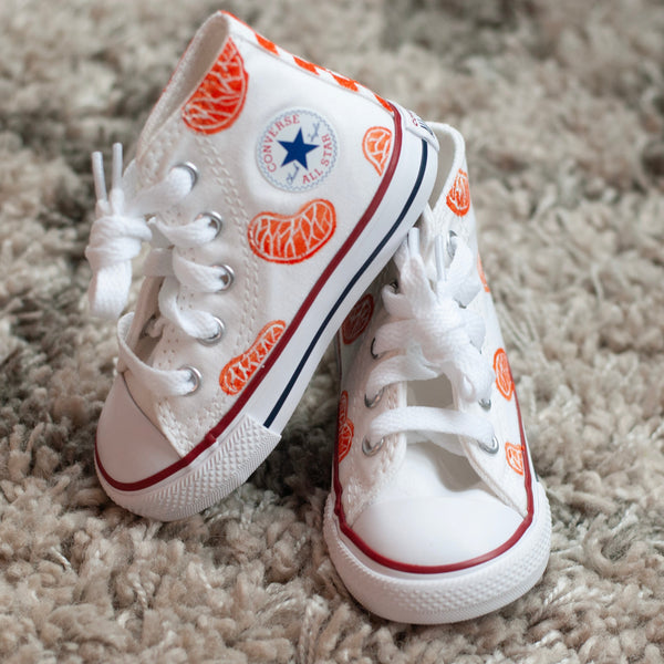 white high top converse with orange slices painted on with an orange checkered back.