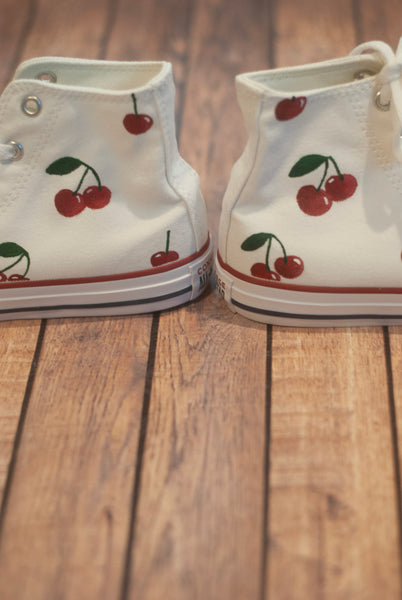 White high-top sneakers with cherry designs on a wooden floor