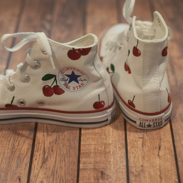 White Converse All Star high-top sneakers with cherry designs on a wooden floor.