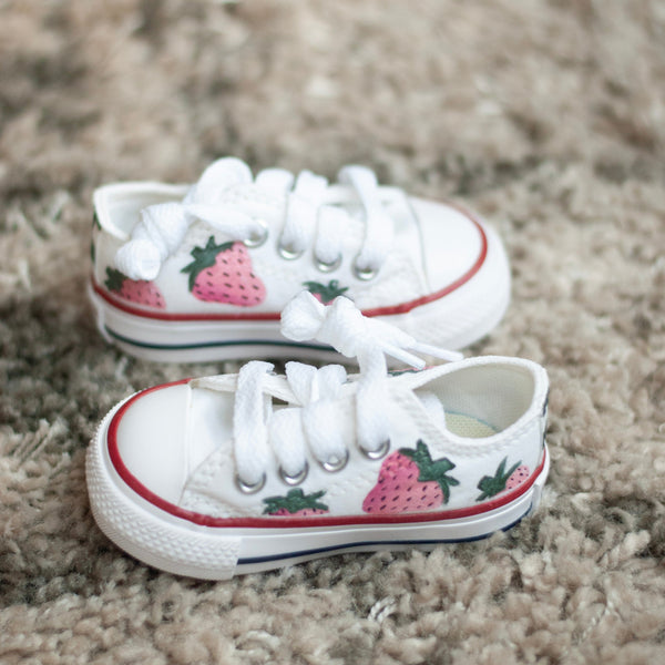 White sneakers with strawberry design on a carpeted floor