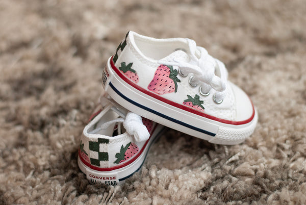 White sneakers with strawberry design on a beige carpet