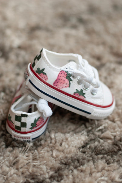 White baby shoes with strawberry design on a carpeted floor