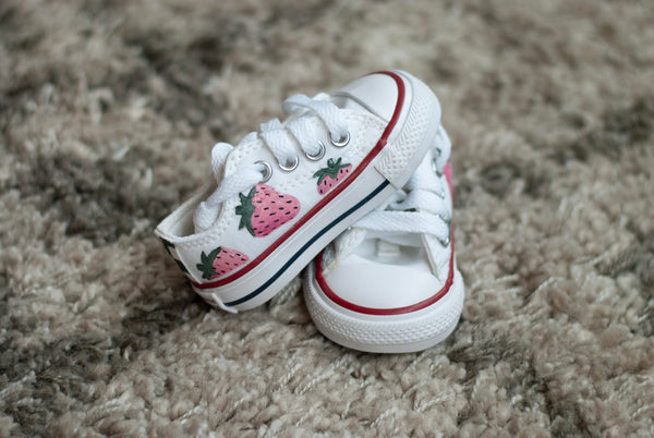 White sneakers with strawberry design on a textured surface