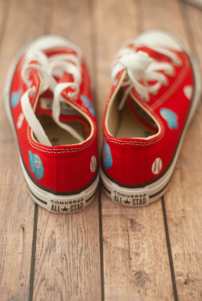Red sneakers with white laces and small blue baseball hats on a wooden floor