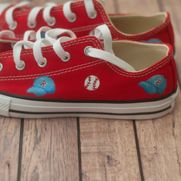 Red sneakers with white laces and small blue baseball hats on a wooden floor