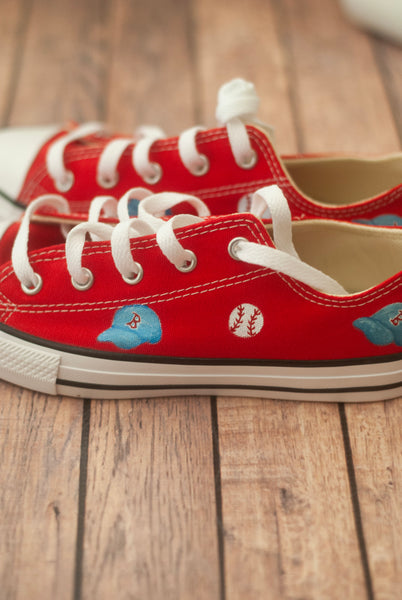 Red sneakers with white laces and small blue baseball hats on a wooden floor