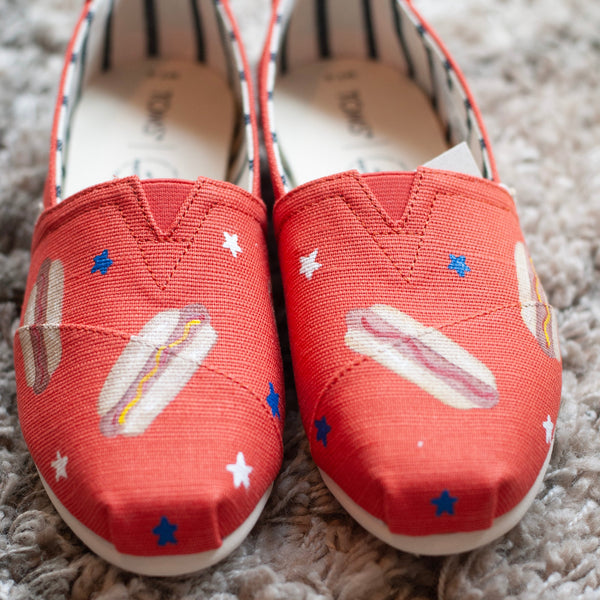 Red slip-on shoes with hot dog design on a gray carpet