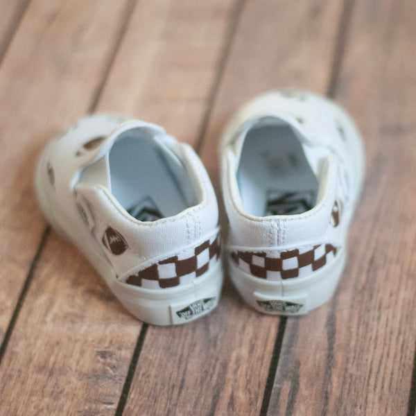 white slip on vans with footballs painted on. A brown checkered print is painted on the back. 