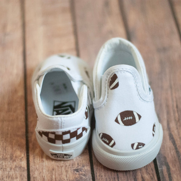white slip on vans with footballs painted on. A brown checkered print is painted on the back. 