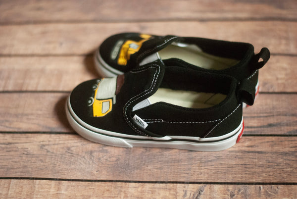 Black children's shoes with yellow trucks on a wooden surface