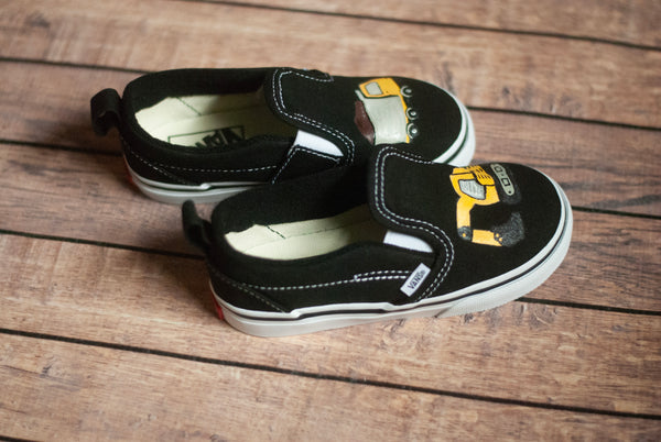 Black slip-on shoes with yellow and white designs on a wooden surface
