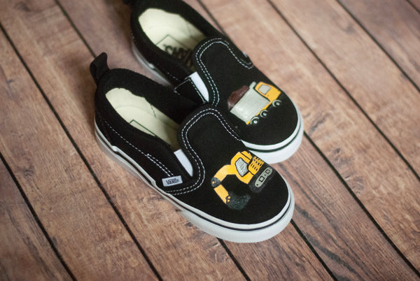 Black slip-on shoes with yellow truck design on a wooden surface