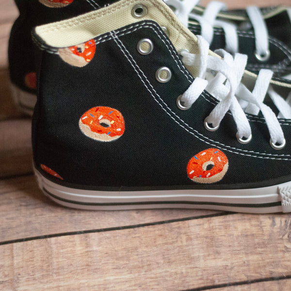 Black high-top sneakers with orange donut designs on a wooden floor