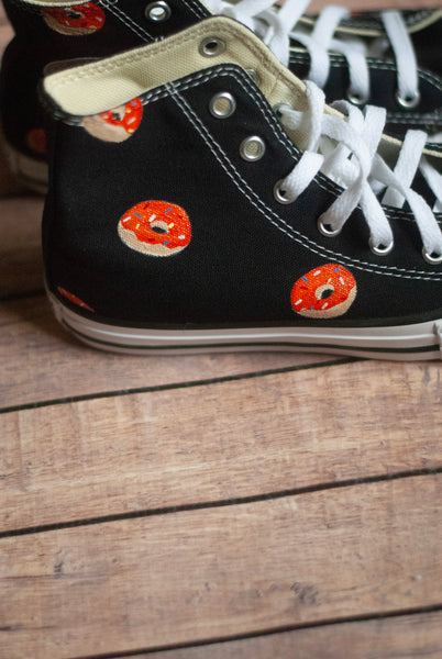 Black high-top sneakers with orange donut designs on a wooden floor