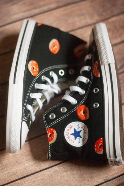 Black high-top sneakers with orange donut pattern on a wooden floor
