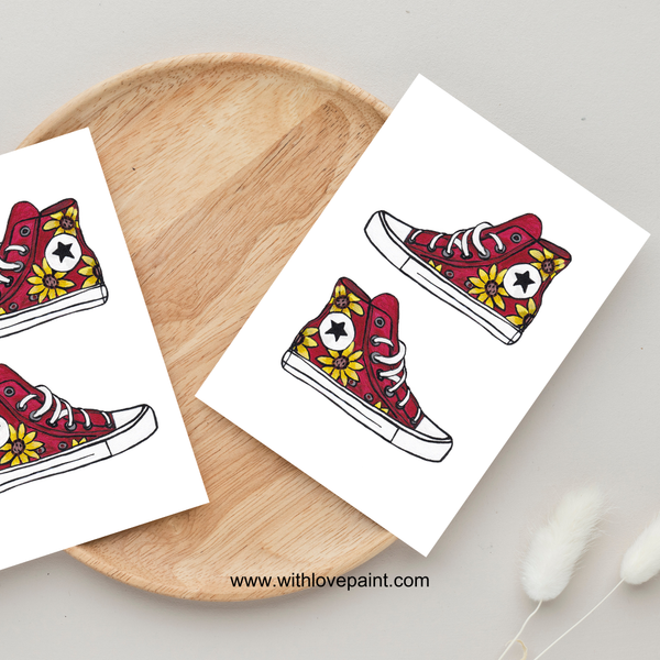 Red high-top sneakers with floral patterns on white cards, placed on a wooden surface.