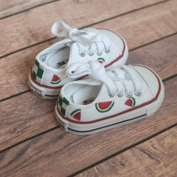 Pair of white sneakers with watermelon slices hand-painted on a wooden floor surface