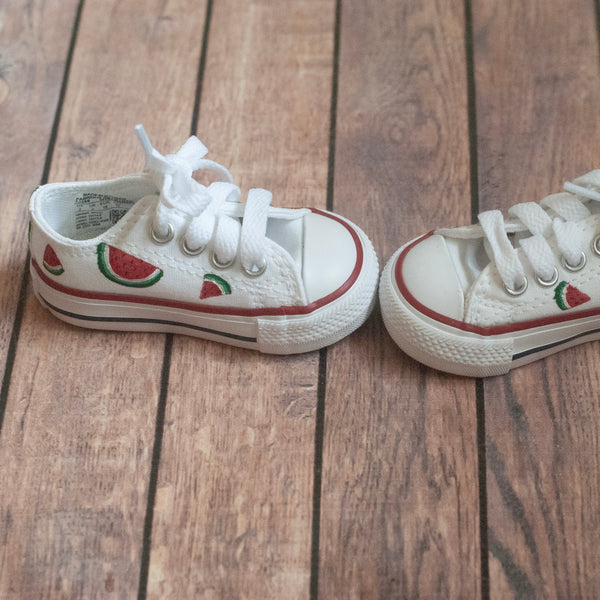 Pair of white sneakers with watermelon slices hand-painted on a wooden floor surface