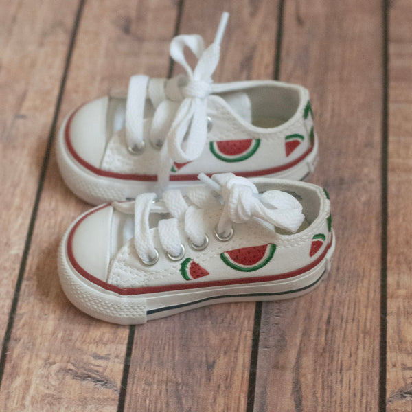 Pair of white sneakers with watermelon slices hand-painted on a wooden floor surface