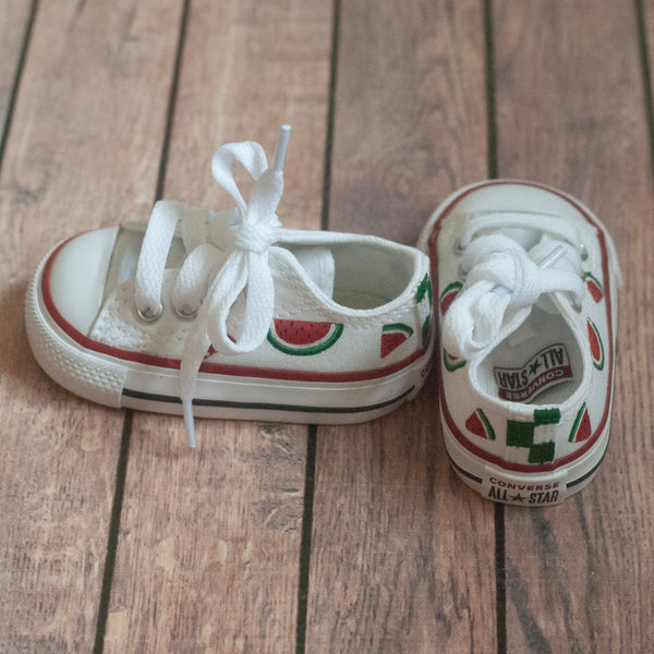 Pair of white sneakers with watermelon slices hand-painted on a wooden floor surface